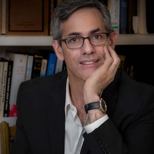 David Myers, looking toward the camera with a slight smile, seated in front of a background of books; he is wearing a white shirt and black suit jacket.